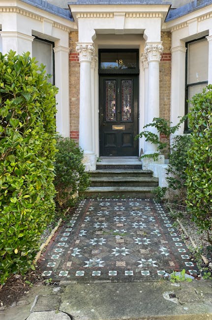 A well-maintained front garden featuring a lush, neatly trimmed lawn with vibrant green grass. In the foreground, a dense cluster of broad, dark green hosta leaves contrasts with the soft, verdant gra
